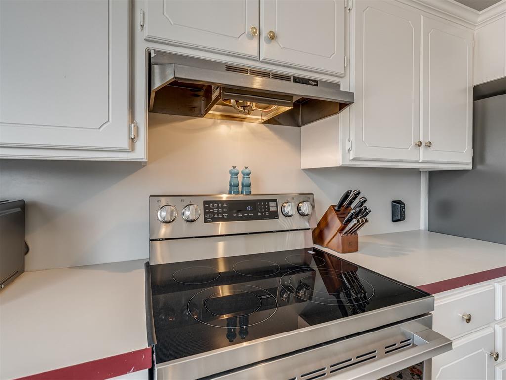 Kitchen range with a black glass cooktop, stainless hood, white cabinets, and a wooden knife block.