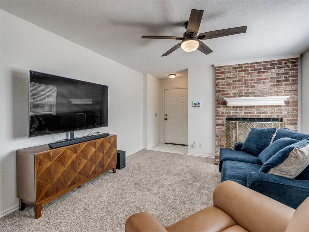 Living room with a brick fireplace, blue sofa, wall-mounted TV, and ceiling fan.