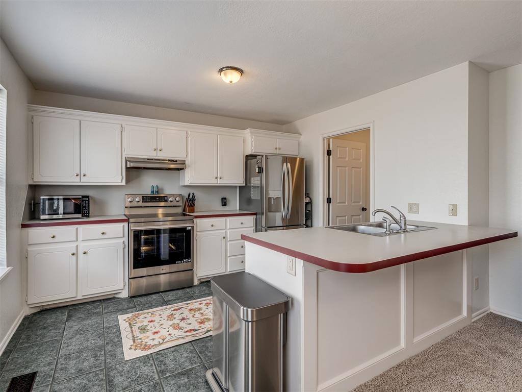 Kitchen with white cabinets, stainless steel appliances, and a sink peninsula with a red-edged counter.