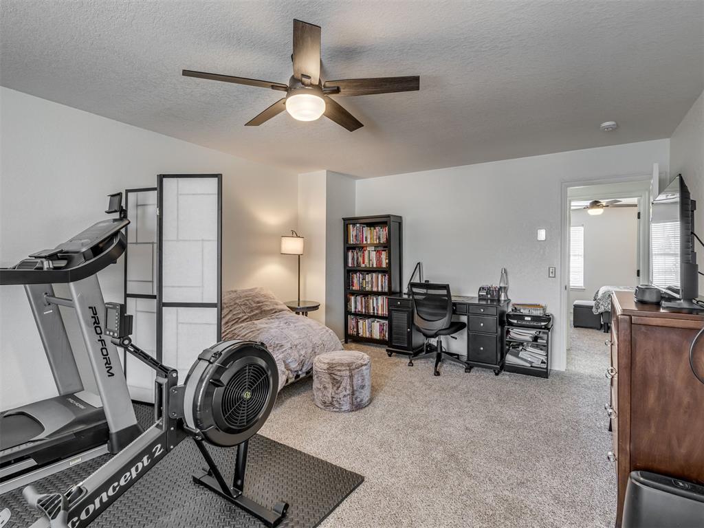 Furnished bedroom and workout room with exercise equipment, a desk, and an open doorway to another bedroom.