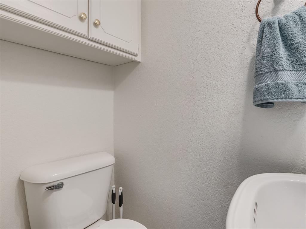 Bathroom with a white toilet, bathtub edge, wall cabinet, and blue towel.
