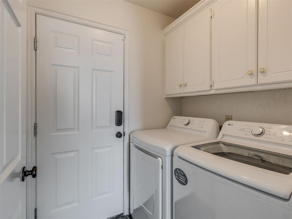 Laundry room with a front-loading washer and dryer beneath white cabinets.