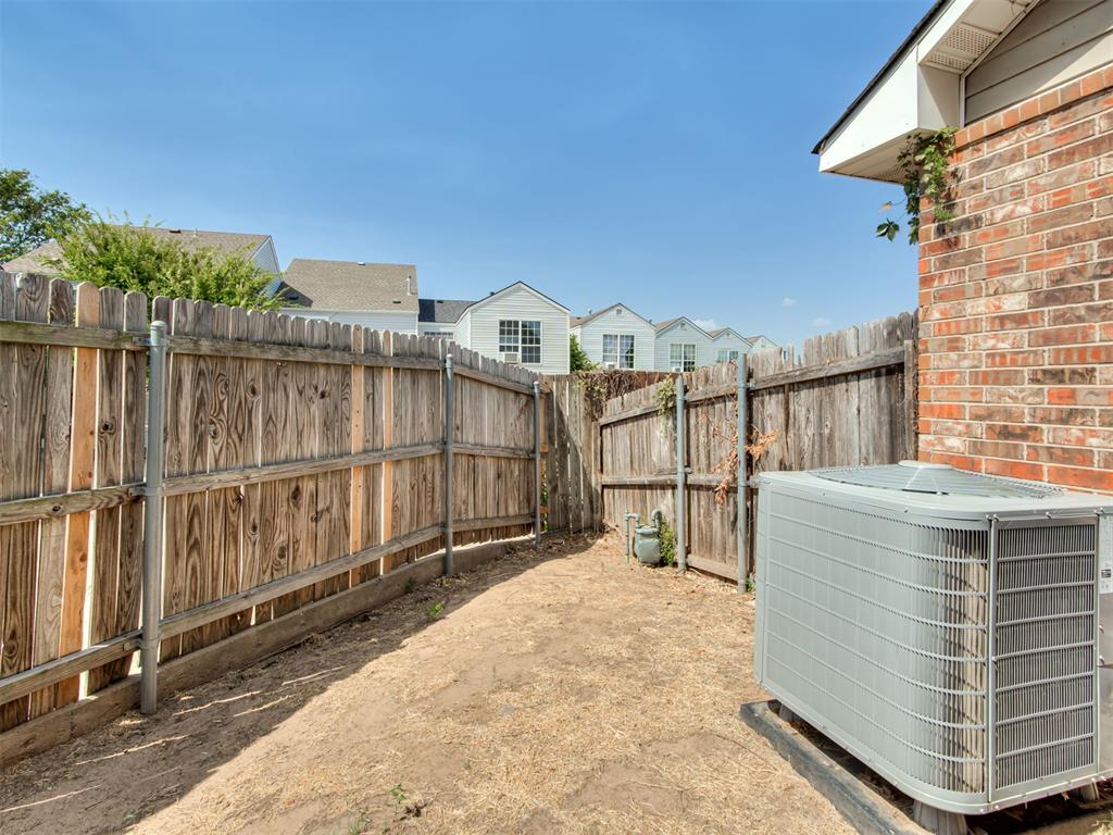 Fenced side yard with bare ground and a large outdoor air-conditioning unit beside a brick wall.