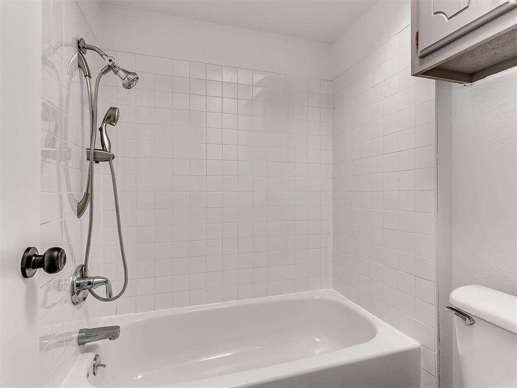 Bathroom with a white tub, tiled surround, and chrome handheld shower.
