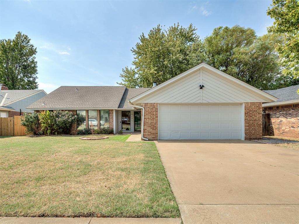 Single-story brick house with a white double garage door, concrete driveway, and front lawn.