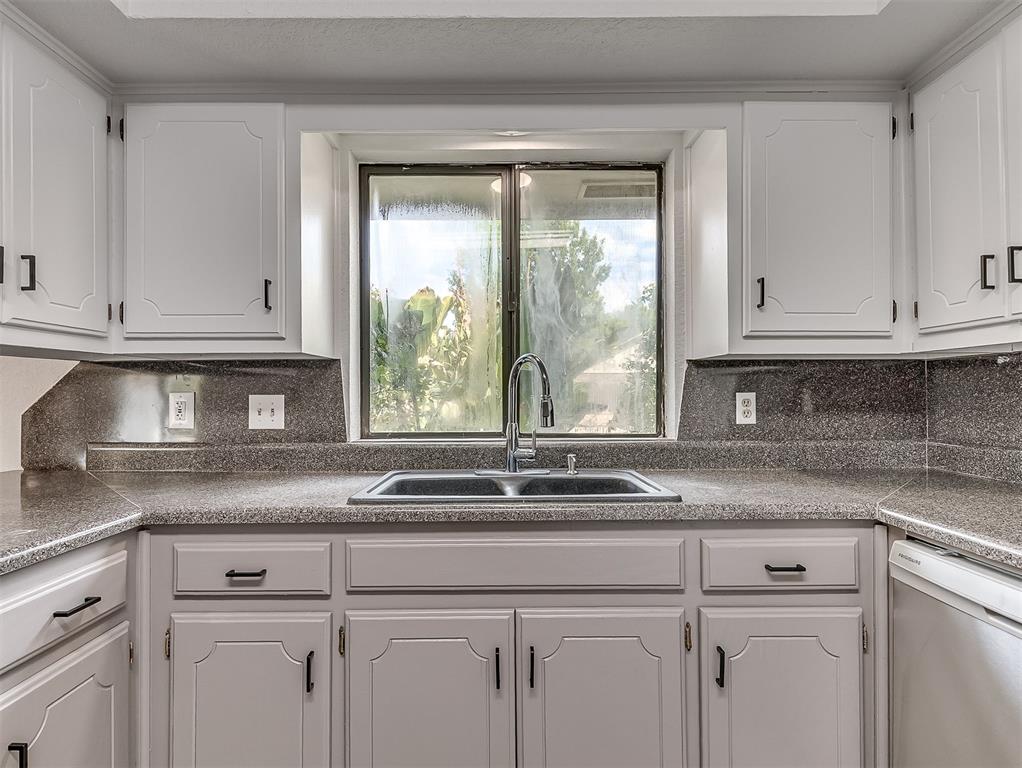 Kitchen with white cabinets, dark speckled counters, and a double-basin sink beneath a window.
