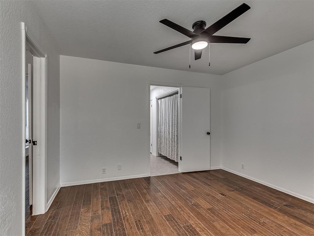 Empty room with dark wood-look flooring and a black ceiling fan; doorway opens to a tiled area.