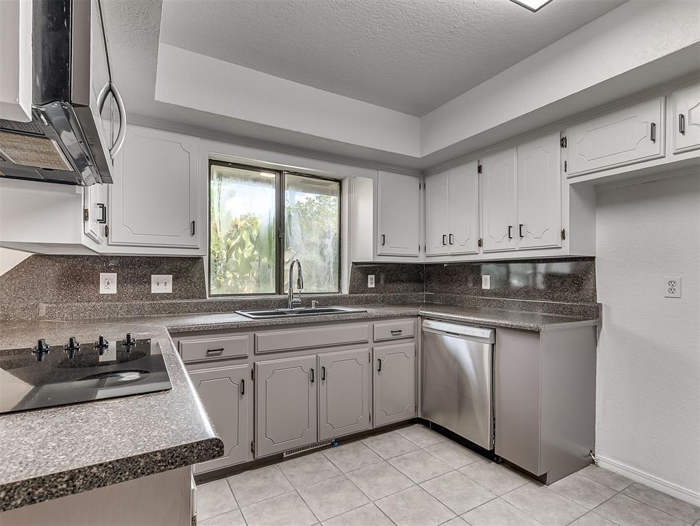 Kitchen with white cabinets, dark speckled counters, a window over the sink, and a stainless-steel dishwasher.
