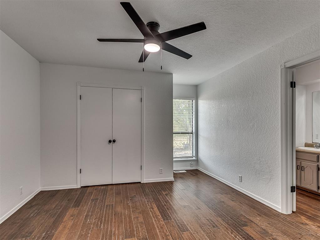 Empty bedroom with dark wood floors, a black ceiling fan, double closet doors, and a window.