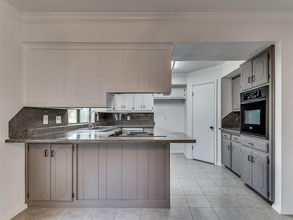 Vacant kitchen with gray paneled cabinets, dark granite counters, a breakfast bar, and a built-in wall oven.