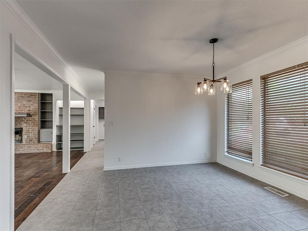 Empty dining area with gray tile floors, a chandelier, and wide windows with wood blinds.