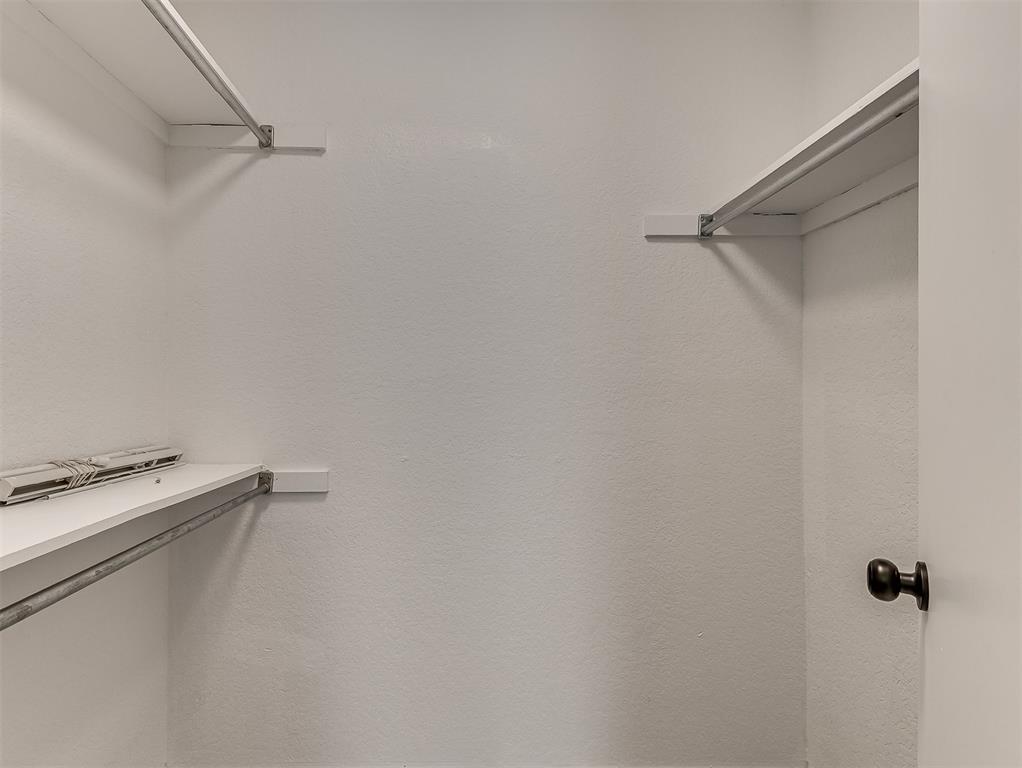 Empty walk-in closet with white shelving and hanging rods along the side walls.
