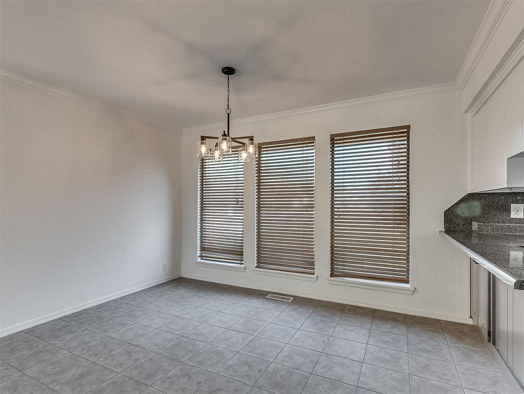 Empty dining area with gray tile floors, three blind-covered windows, and a chandelier.
