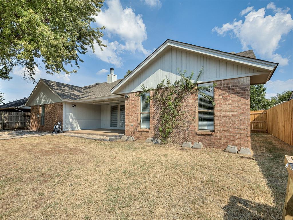 Brick home’s rear exterior with a covered patio and fenced backyard.