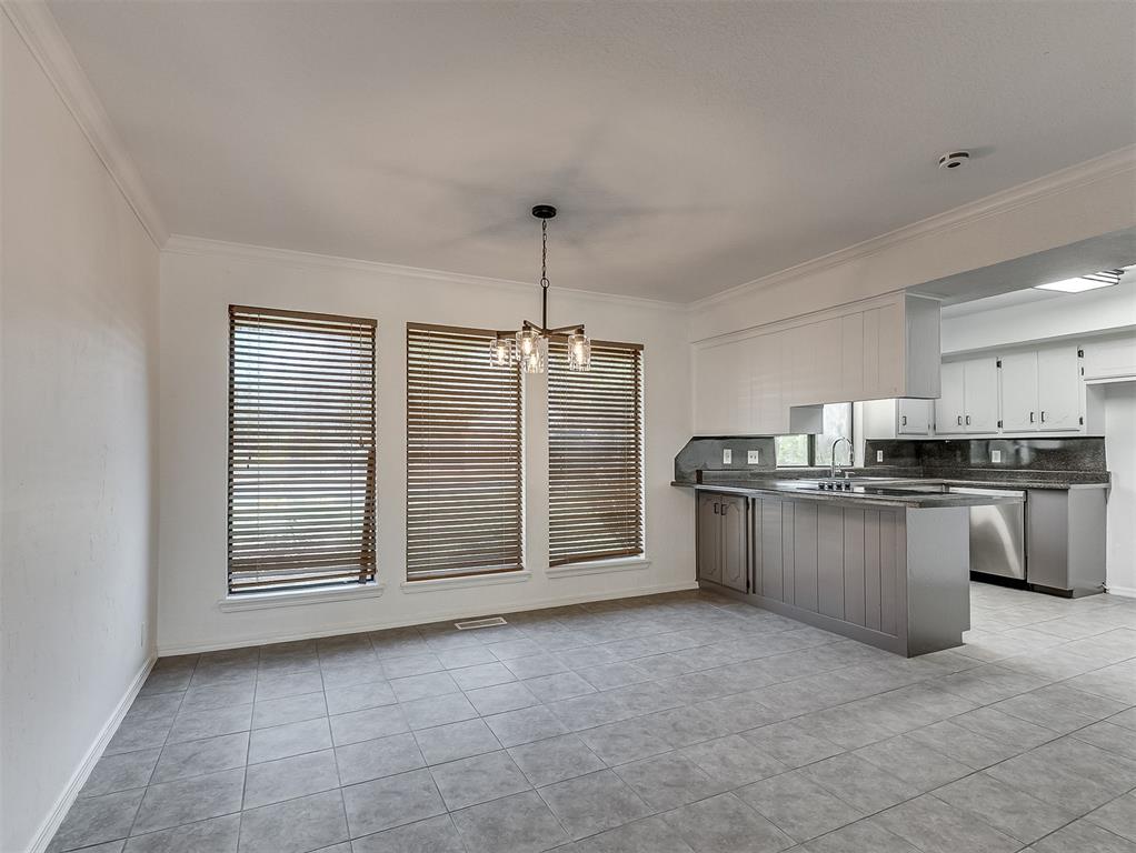 Open dining area and kitchen with a gray island, tiled floors, and three windows with wooden blinds.