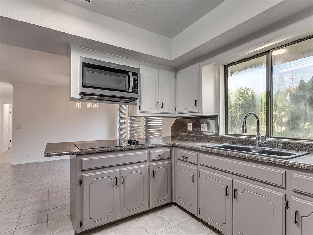 Kitchen with white cabinets, dark countertops, and a double-basin sink beneath a large window.