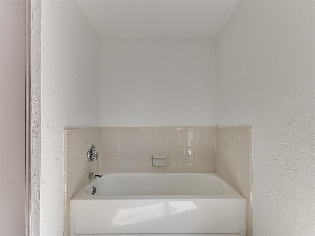 White alcove bathtub with cream tile surround and chrome fixtures.
