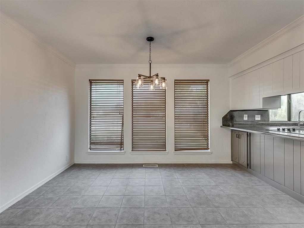Empty dining area with three blinded windows, a chandelier, tiled floors, and adjoining gray kitchen cabinets.
