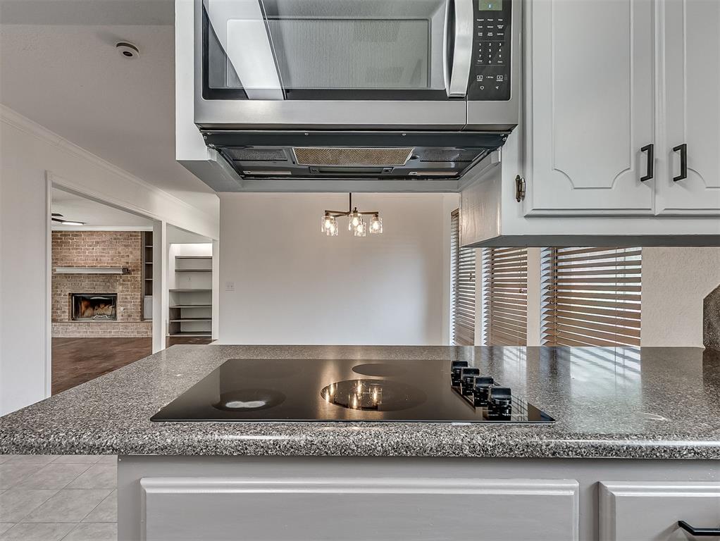 Kitchen with granite peninsula and cooktop, stainless-steel microwave, and a brick fireplace visible beyond.