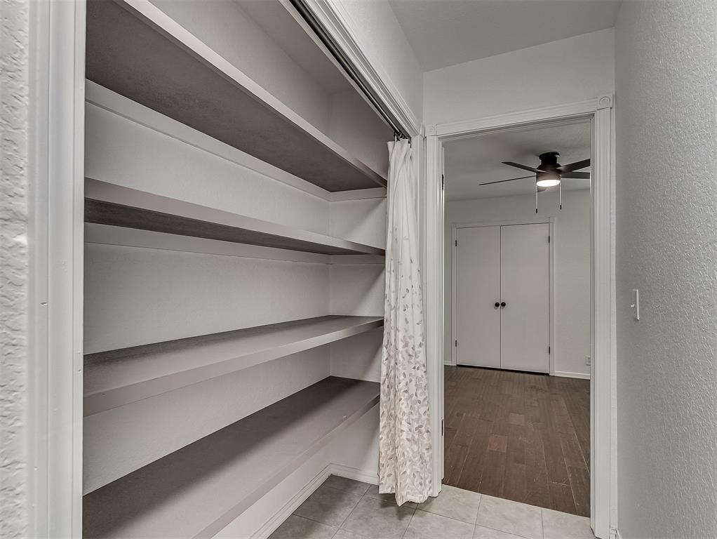 Walk-in closet with long built-in shelves and a curtain beside a doorway to an empty room.