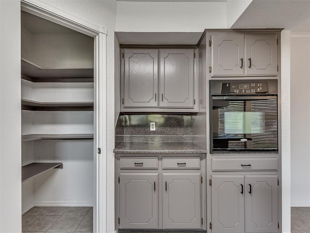 Kitchen with gray cabinets, built-in oven, speckled counters, and open pantry shelving.