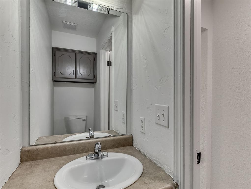 Bathroom vanity with an oval sink and mirror reflecting a toilet and wall cabinet.