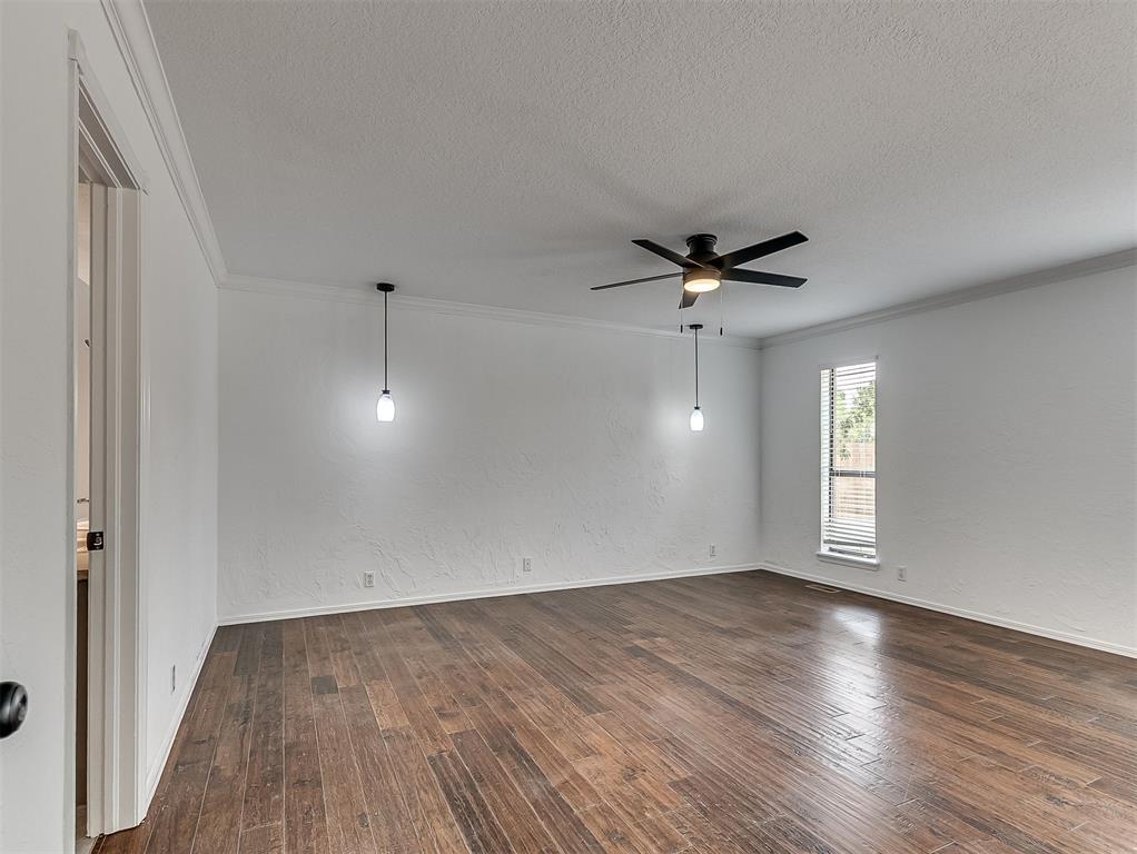 Empty room with dark wood floors, a ceiling fan, pendant lights, and a window with blinds.