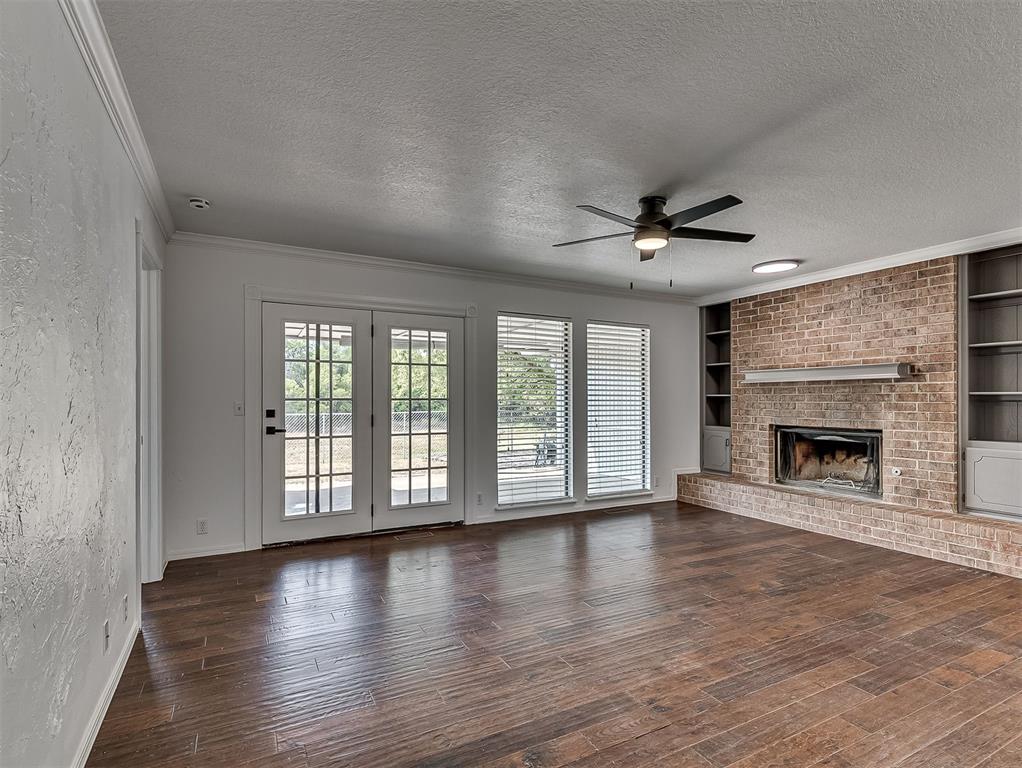 Empty living room with a brick fireplace, built-in shelving, and French doors.