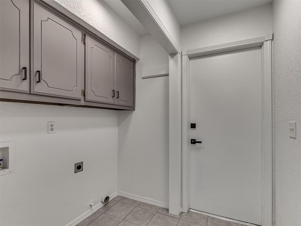 Laundry room with gray upper cabinets, tiled floor, and utility connections beside a white door.