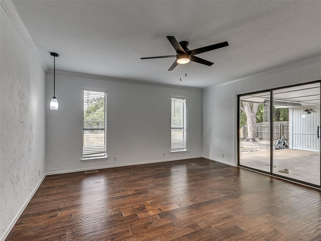 Empty living area with dark wood floors, ceiling fan, and sliding glass doors to a covered patio.