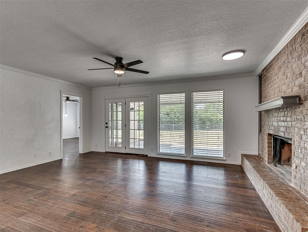 Unfurnished living room with dark hardwood floors, a brick fireplace, and glass doors opening onto patio.