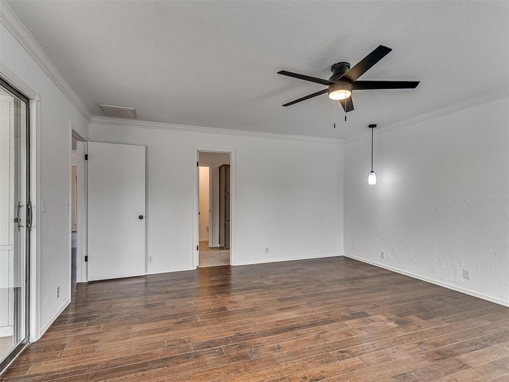 Empty room with plank flooring, a black ceiling fan, and a sliding glass door.