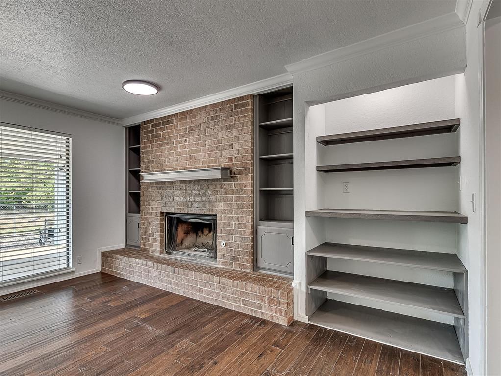 Living room with a brick fireplace, built-in shelves, and dark wood flooring.