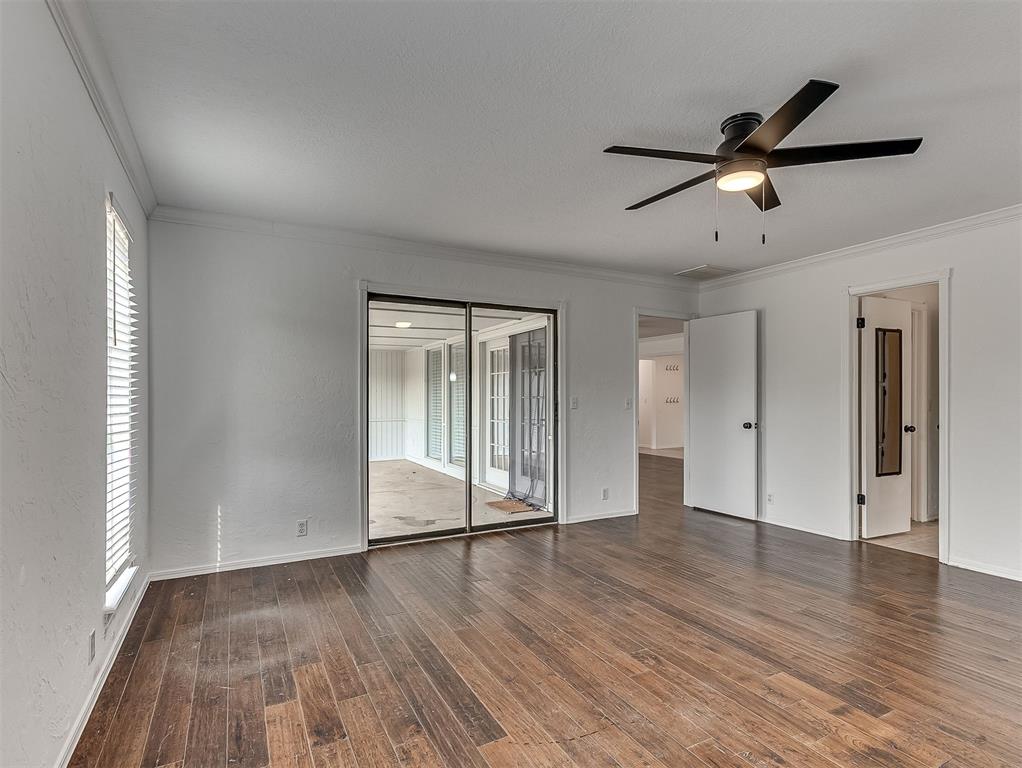 Empty living room with dark wood floors, ceiling fan, and sliding doors to an enclosed sunroom.