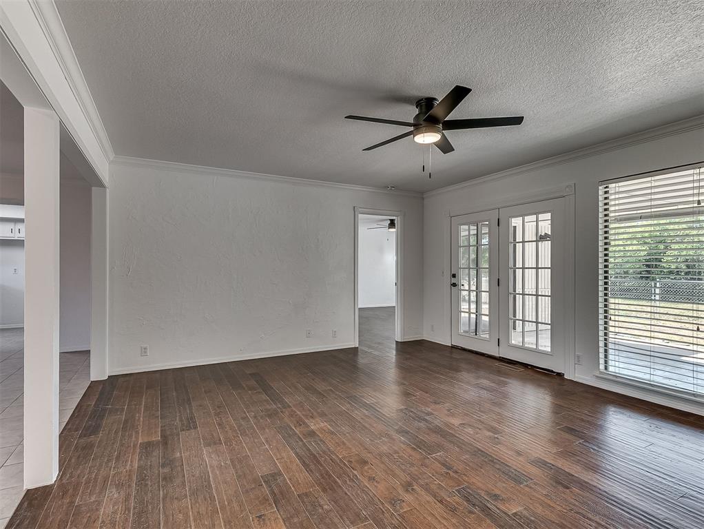 Vacant living room with hardwood floors, French doors, and a black ceiling fan.
