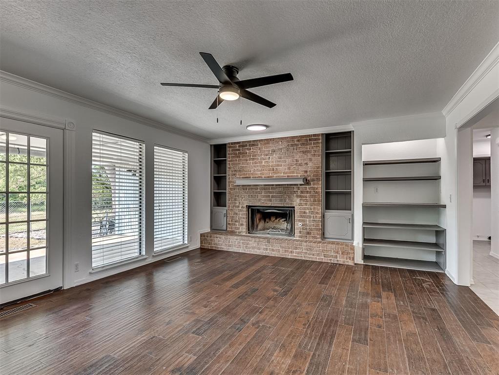 Vacant living room with a brick fireplace, built-in shelving, and dark hardwood floors.