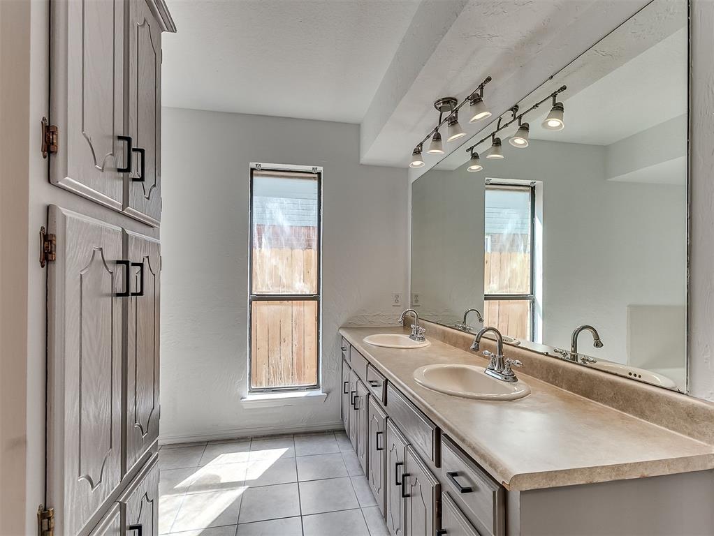 Bathroom with double-sink vanity, large mirror, gray cabinets, and tiled floor.