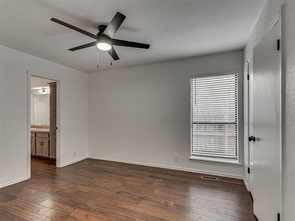 Empty bedroom with dark flooring, a black ceiling fan, and a window with blinds.