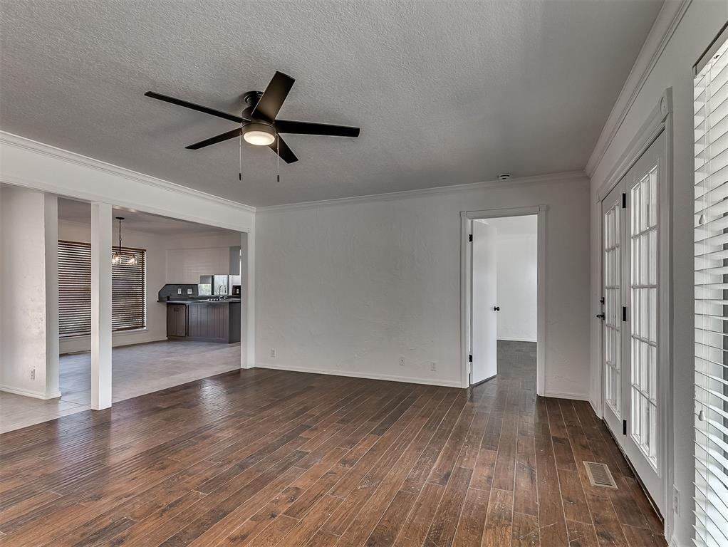 Vacant living room with dark wood floors, ceiling fan, and French doors opening to the kitchen.