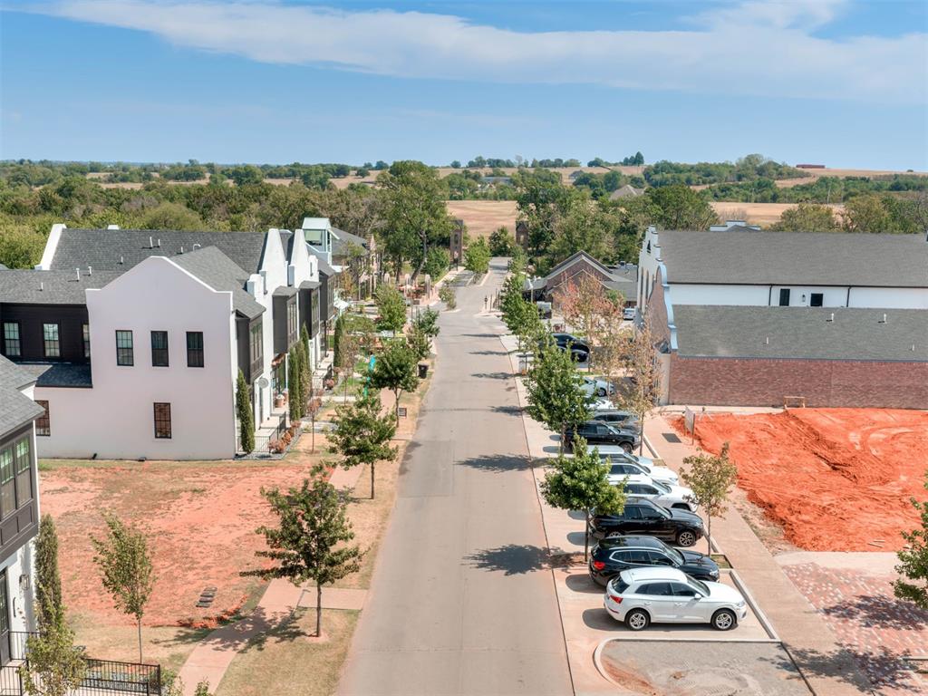 Elevated view down a development street with modern buildings, parked cars, and a red-dirt lot.