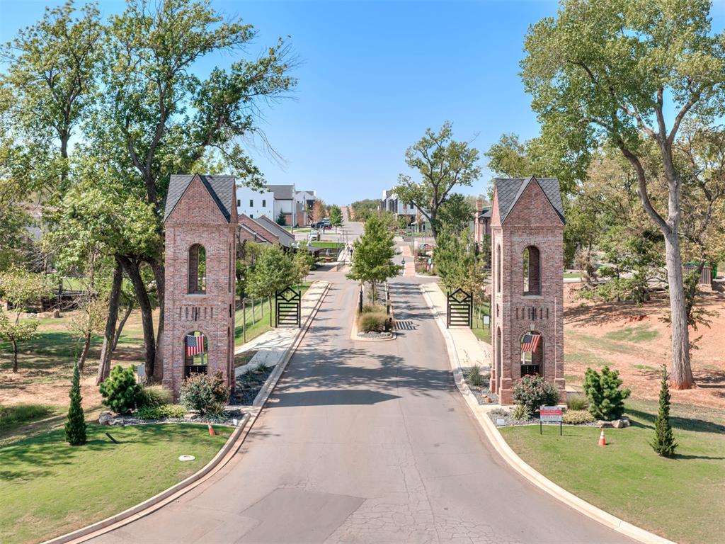 Neighborhood entrance with paired brick towers, open gates, and a tree-lined road.