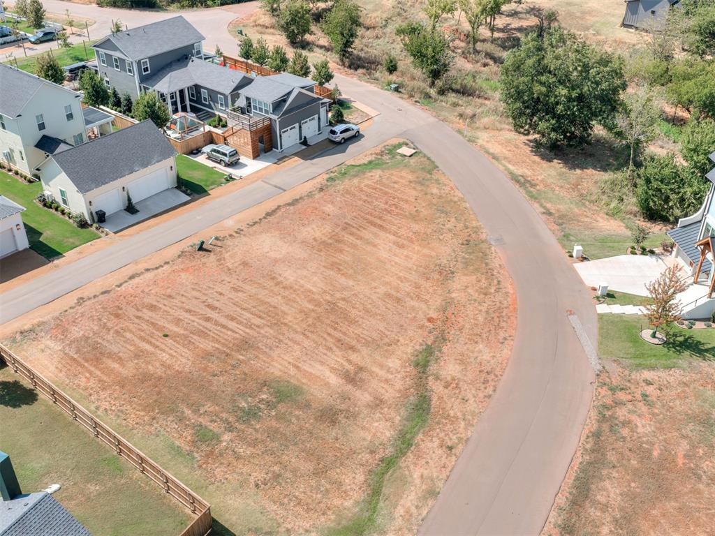Cleared vacant lot beside a curved neighborhood road, with homes and fenced yards nearby.