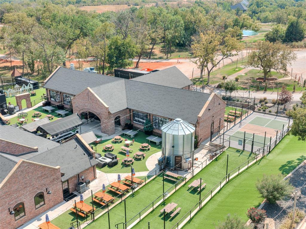 Brick clubhouse and recreation area with picnic tables, turf seating, and fenced sports courts.