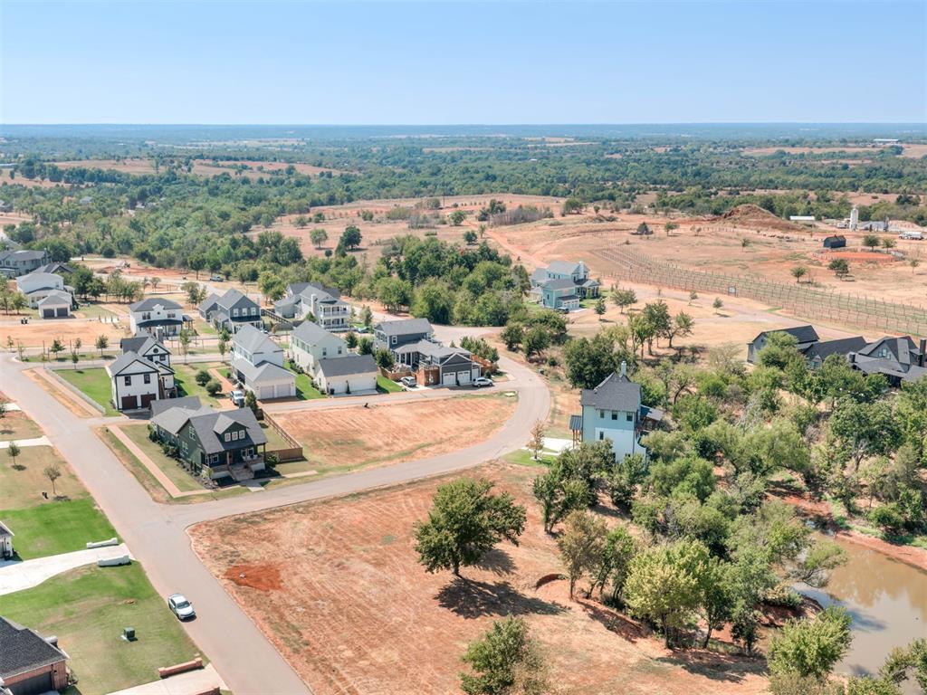 Aerial view of a residential neighborhood with open lots, curving roads, and wooded countryside beyond.
