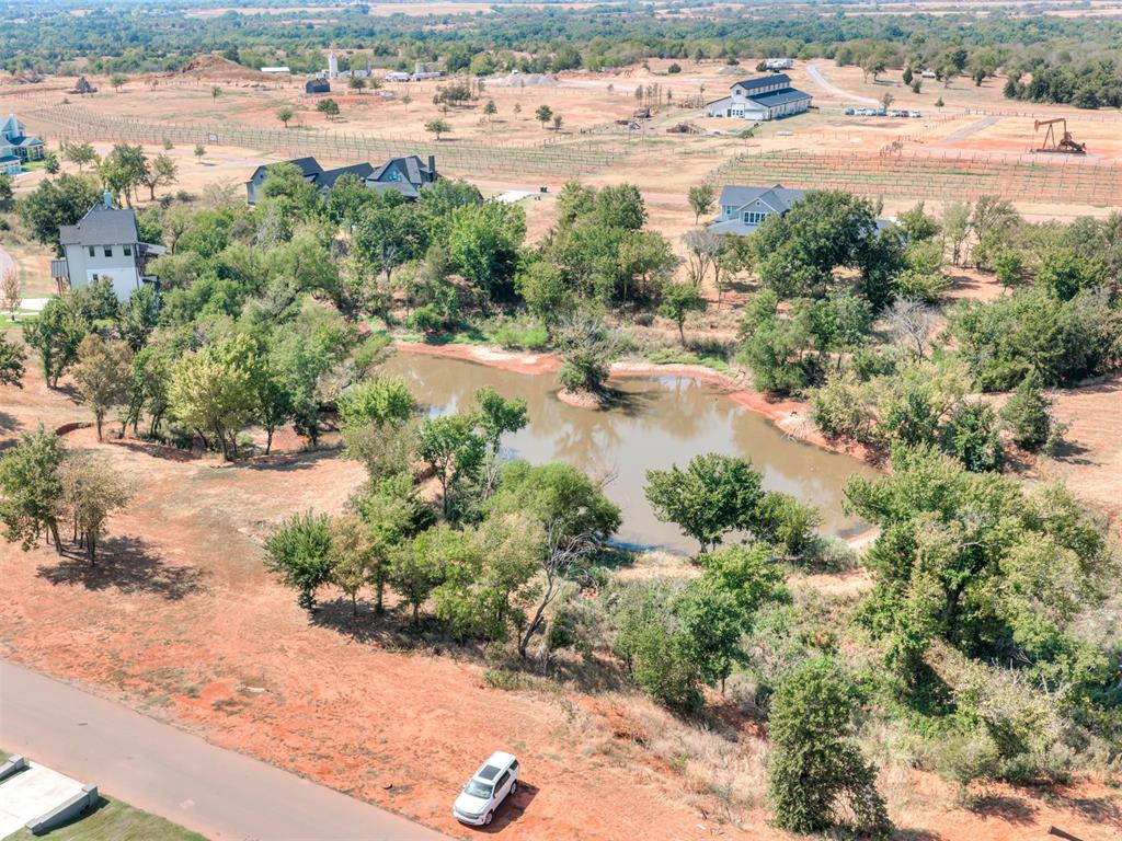 Aerial view of a tree-lined pond, open reddish ground, and homes across the surrounding rural landscape.