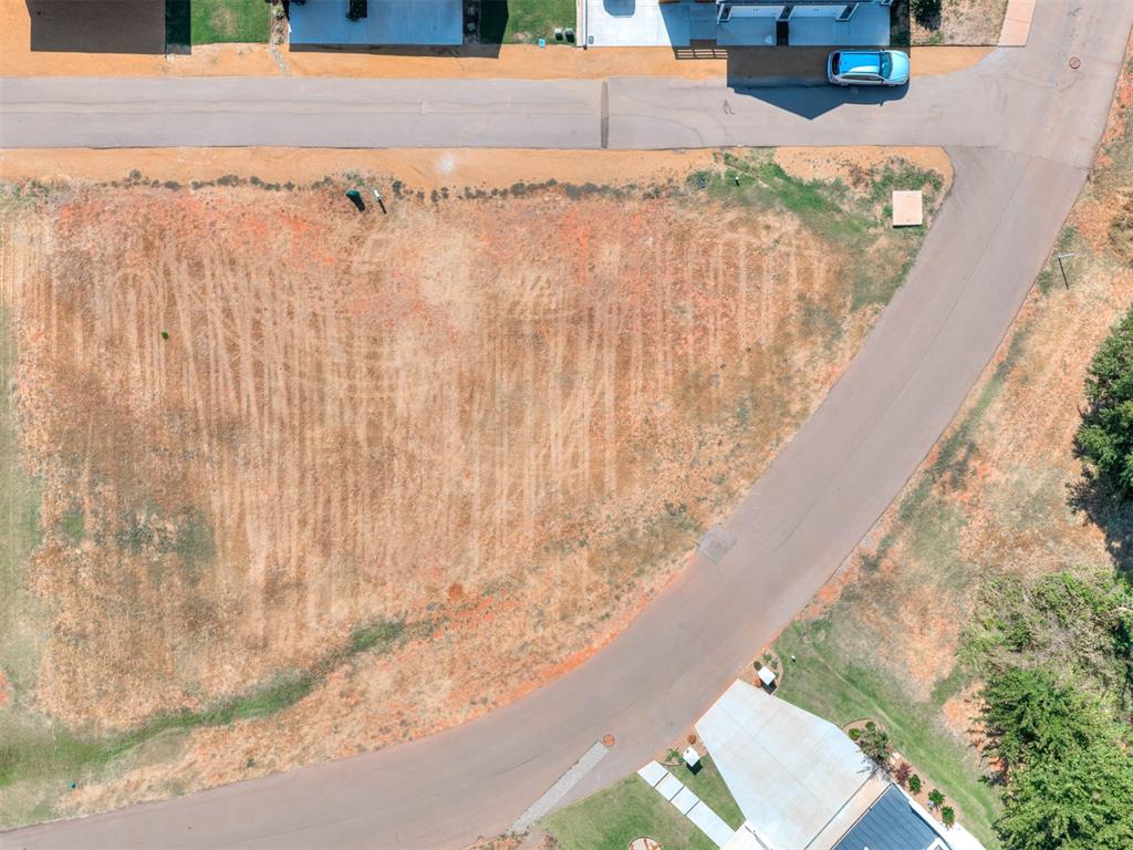 Aerial view of a dry vacant lot beside a curved street, with neighboring homes at the edges.