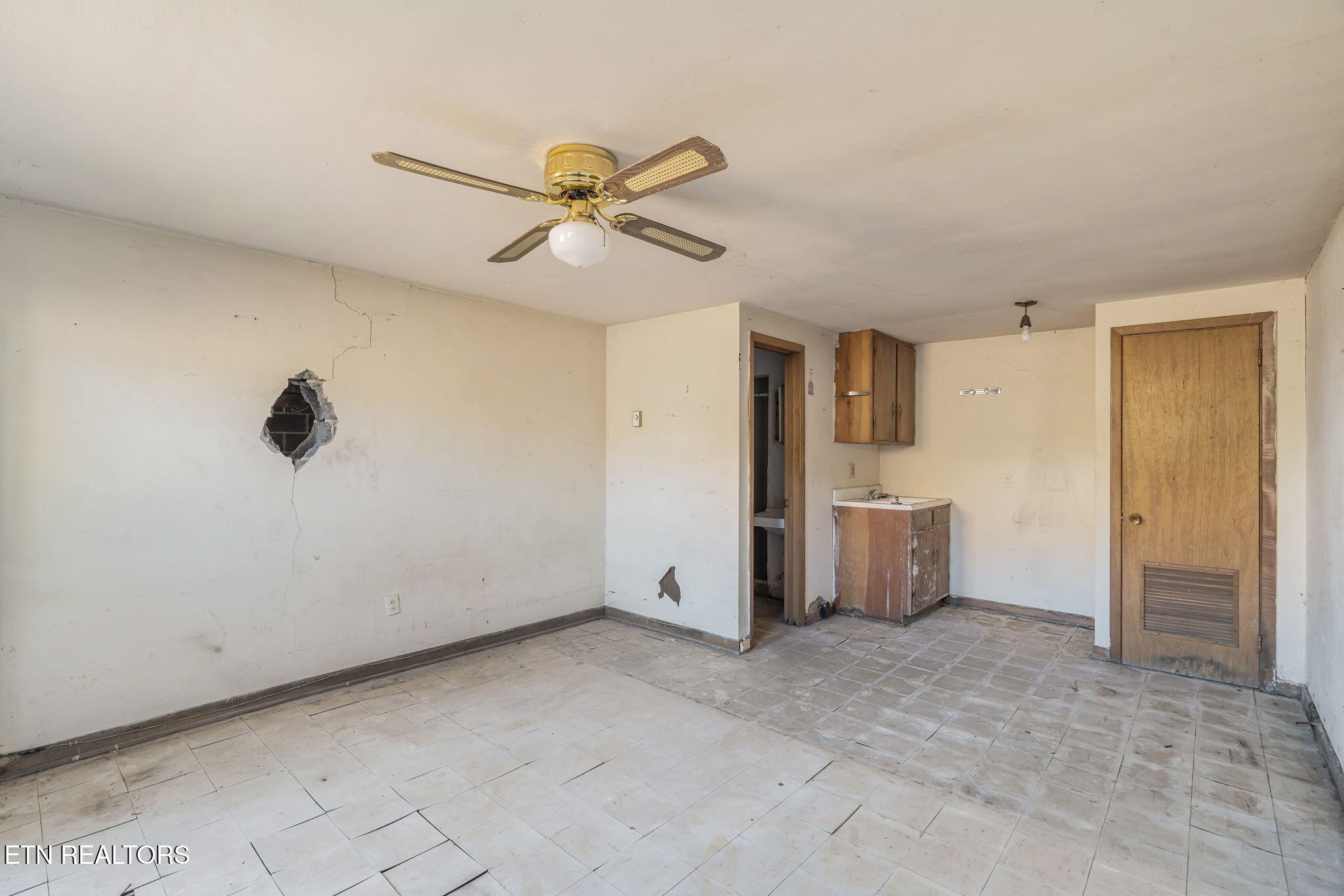 Vacant kitchen with a tiled floor, worn sink and cabinets, and a large hole in the wall.