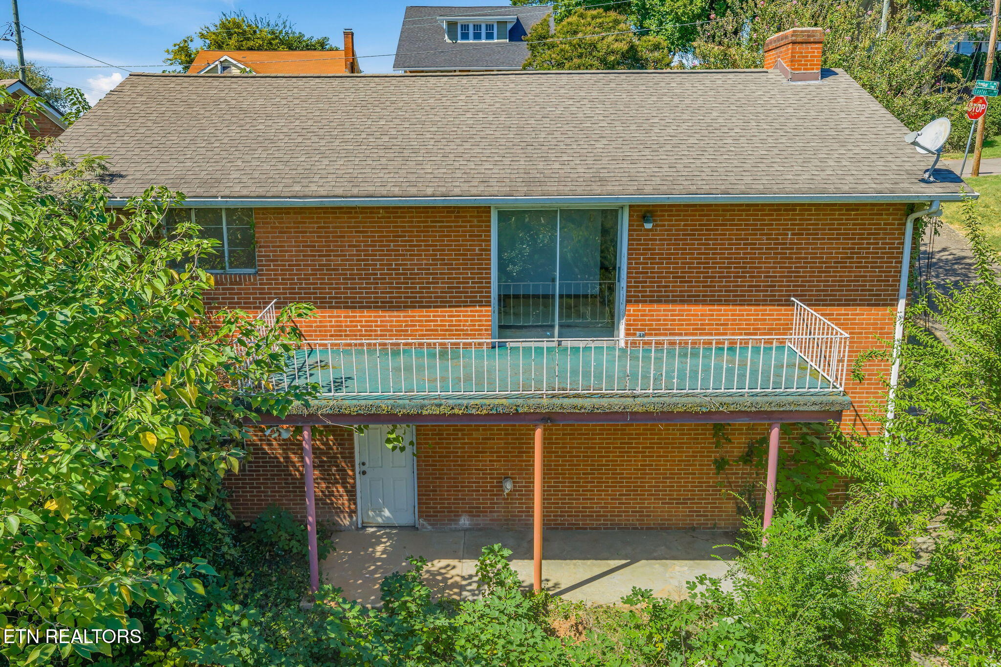 Rear of a red brick house with a raised balcony and covered patio.