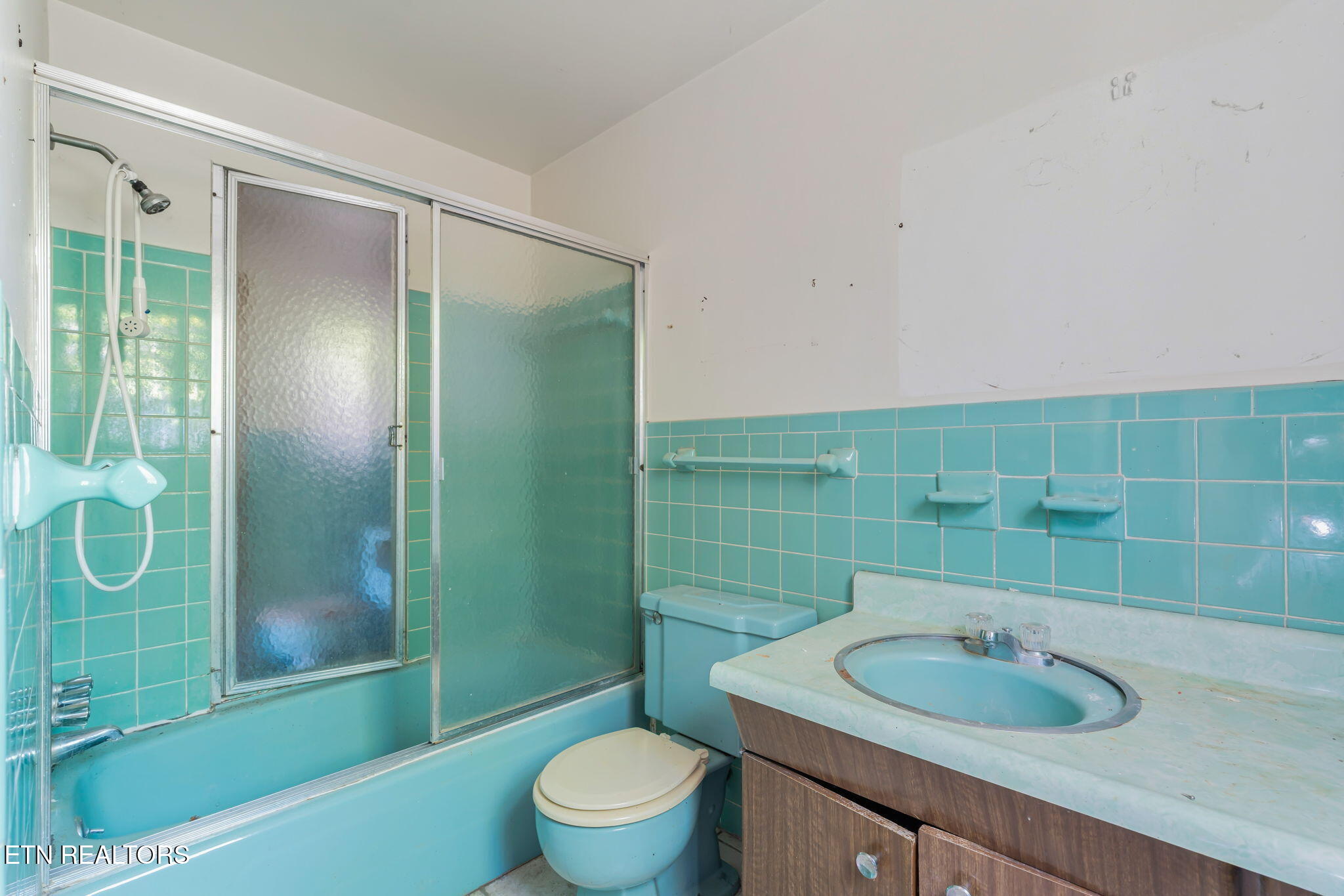 Bathroom with turquoise tile, a glass-enclosed tub and shower, and a matching toilet.