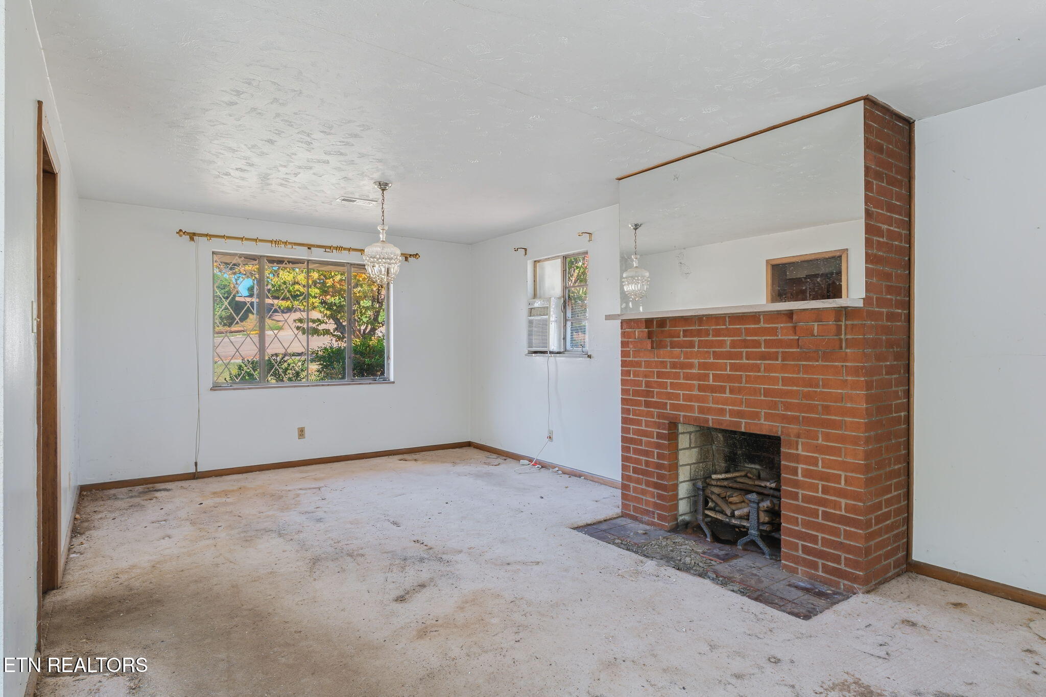 Vacant living room with a red brick fireplace and stained carpet.